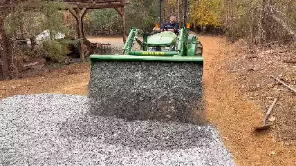 Picture of a landscape contractor using a John Deere tractor to spread gravel on a driveway